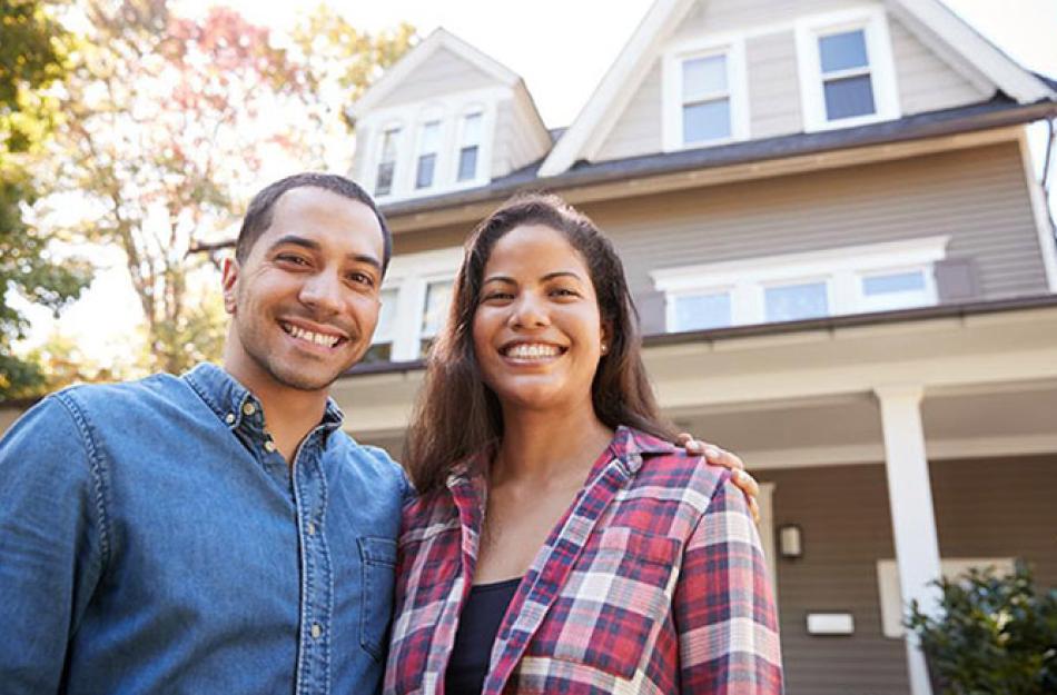 Couple smiling in front of their home.
