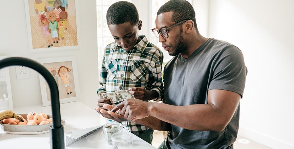 Parent counting money with child in kitchen.